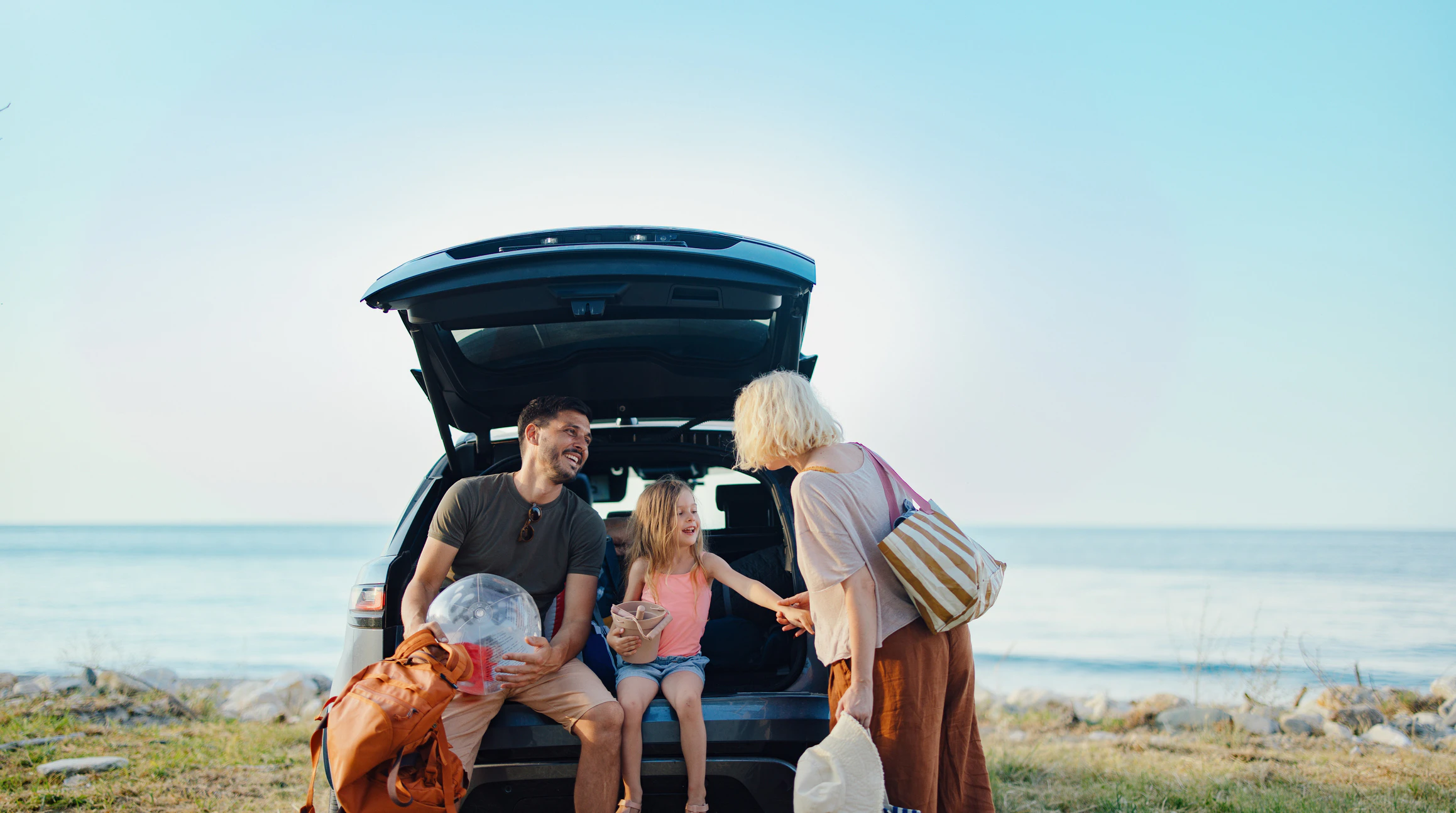 Family unloading their SUV by the water, with parents and a young girl preparing for a day outdoors.