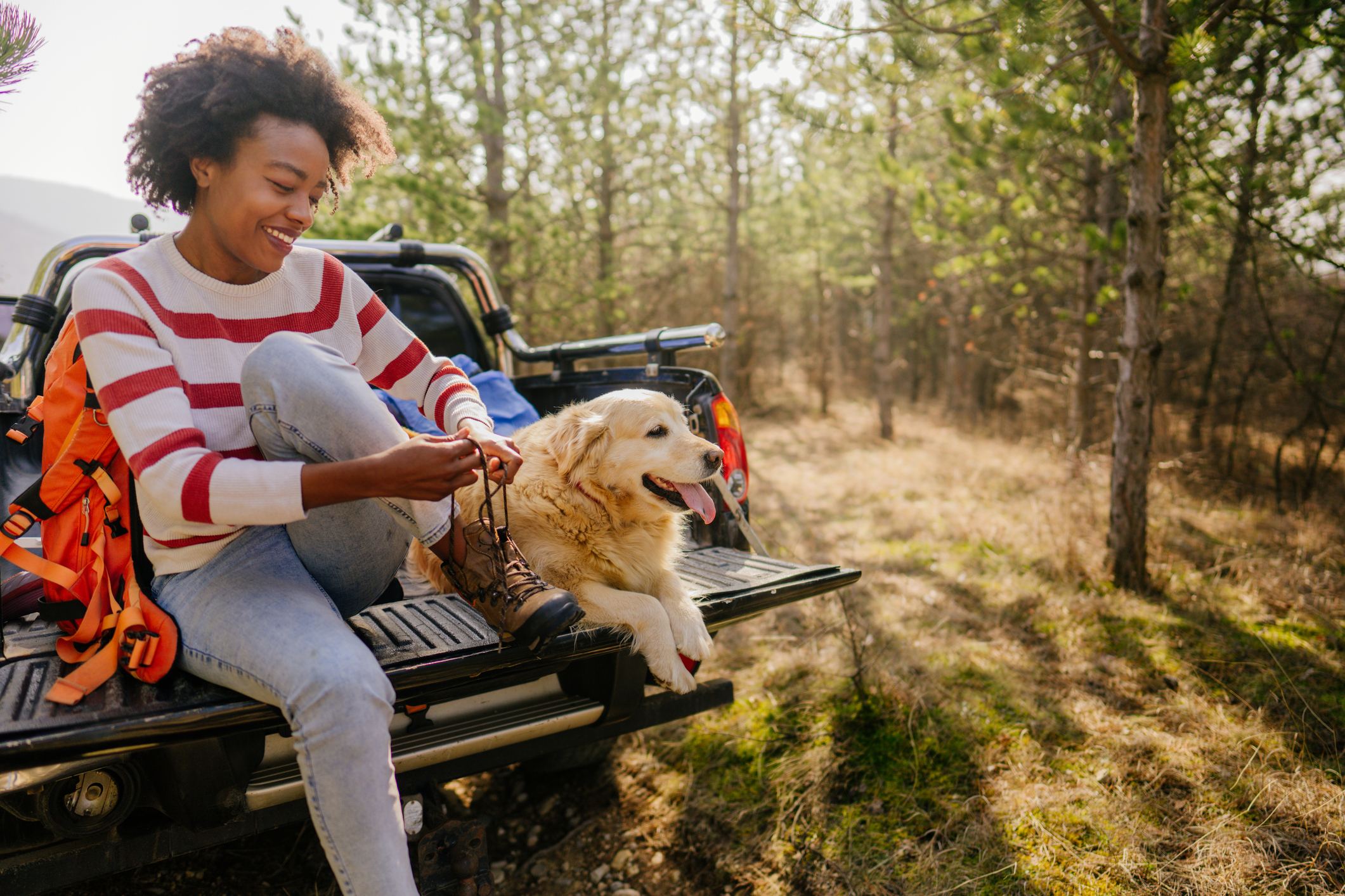 Woman with dog sitting on tailgate of pickup truck on forest trail