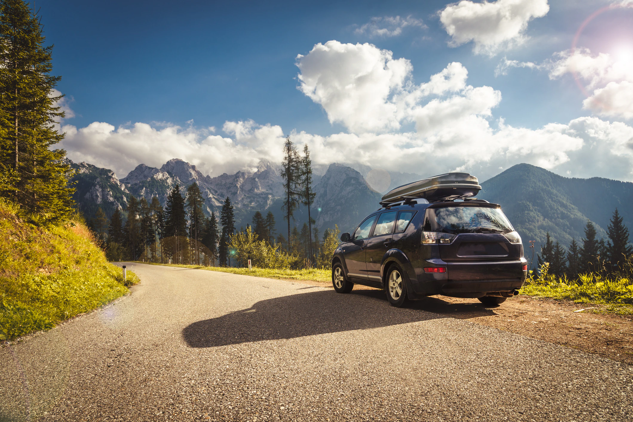 SUV with roof cargo box parked on mountain road with scenic alpine landscape