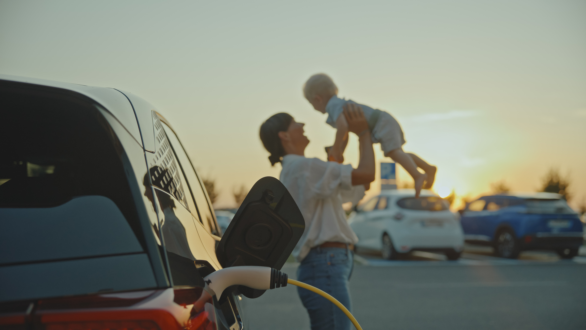 Parent holding child near vehicle in parking lot at sunset