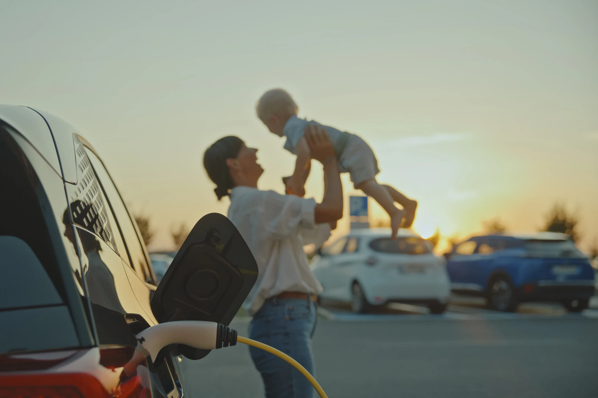 Parent holding child near vehicle in parking lot at sunset