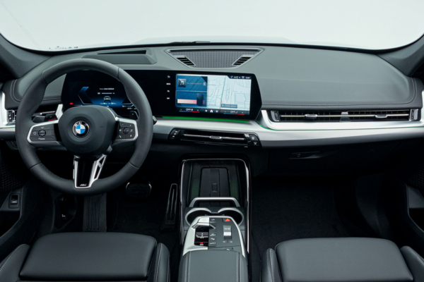 BMW X1 interior featuring a digital instrument display, centre touchscreen, steering wheel, centre console and black leather seats.
