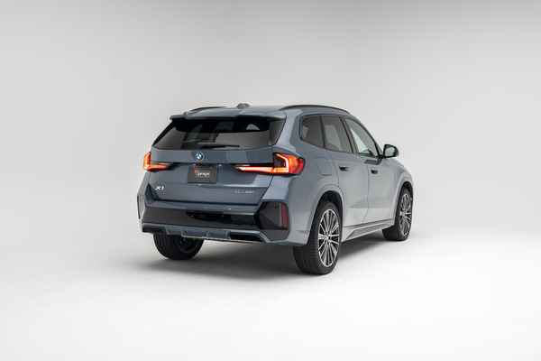 Rear three-quarter view of a grey 2026 BMW X1 xDrive28i SUV on a white studio background.