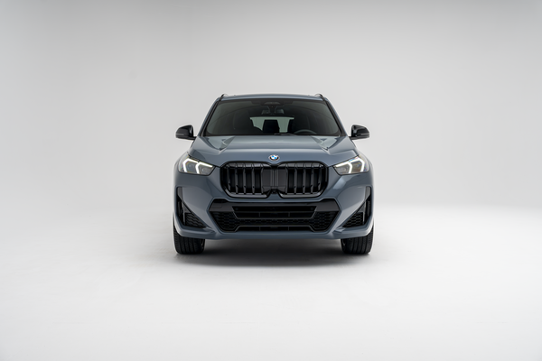 Front view of a grey 2026 BMW X1 xDrive28i SUV with LED headlights illuminated on a white studio background.