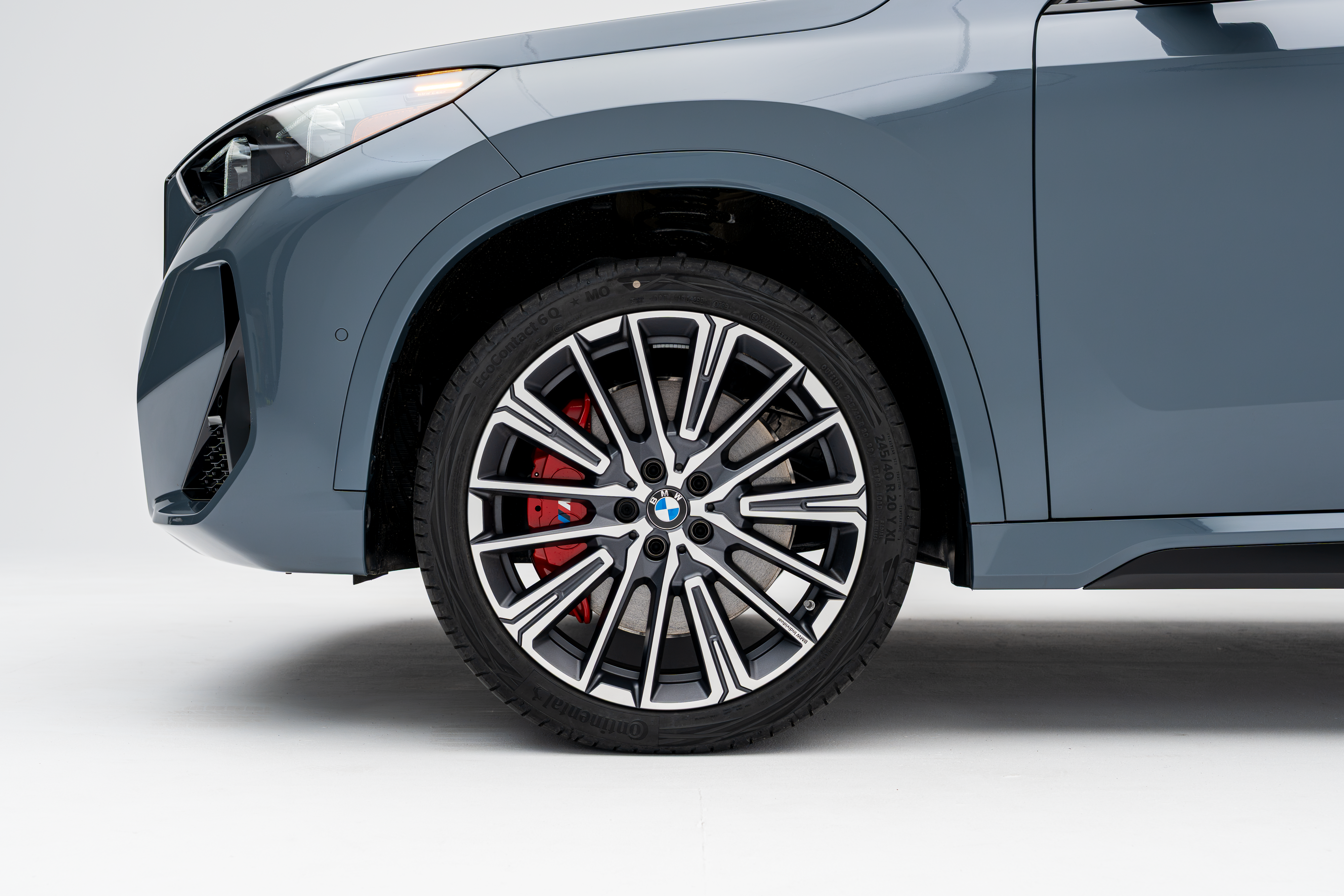 Close-up side view of the front wheel and fender of a grey 2026 BMW X1 xDrive28i, featuring a multi-spoke alloy wheel and red brake caliper.