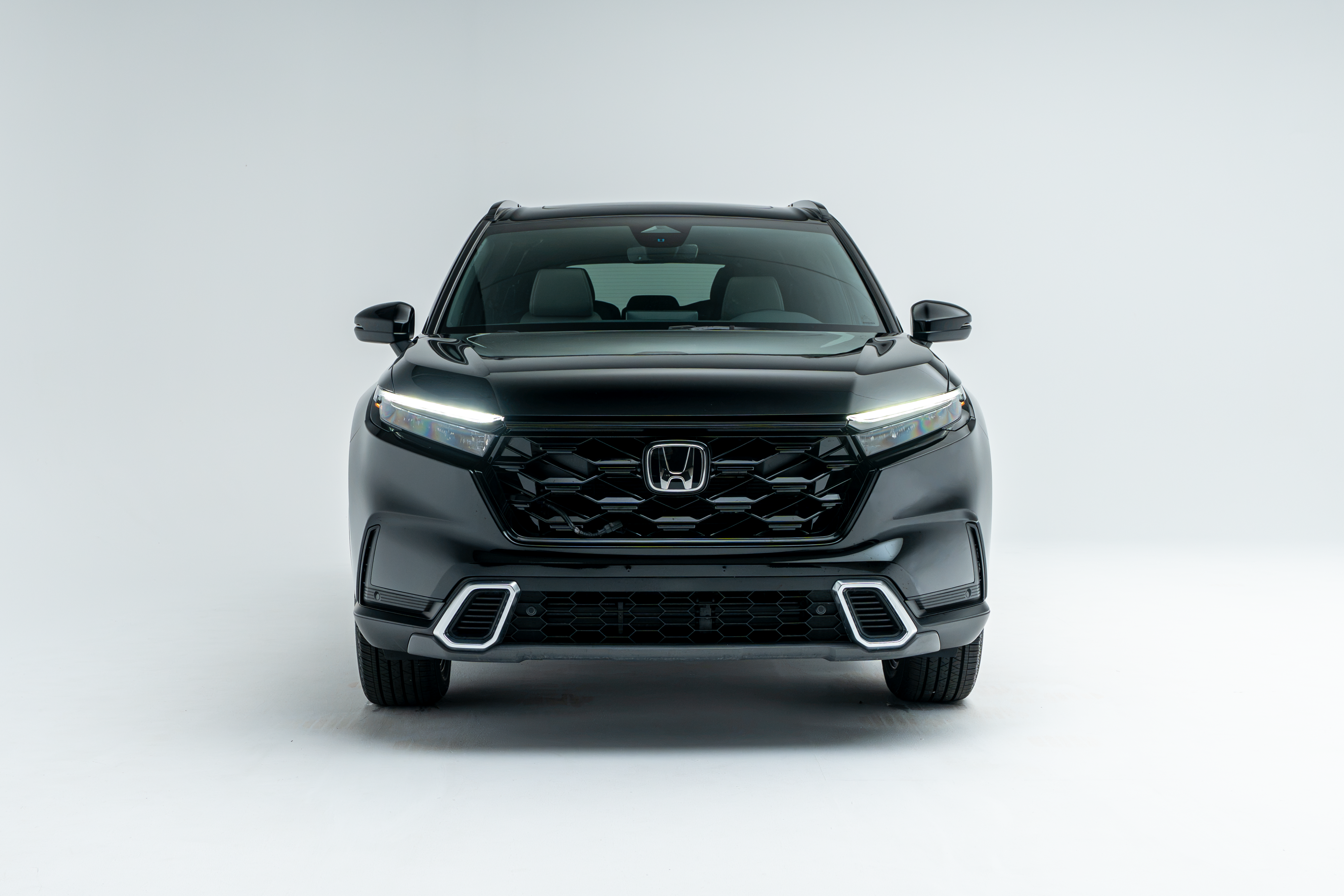 Front view of a black 2026 Honda CR-V SUV with LED headlights illuminated on a white studio background.