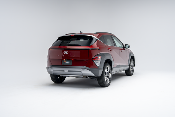 Rear three-quarter view of a red 2026 Hyundai Kona SUV with LED taillights illuminated on a white studio background.