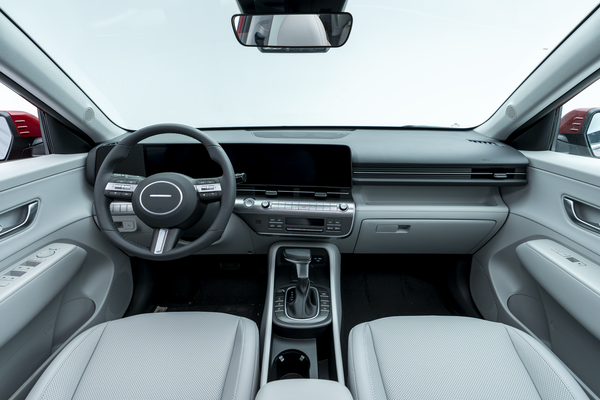 Interior view of a 2026 Hyundai Kona featuring the steering wheel, digital display, dashboard, centre console, and light-coloured front seats.