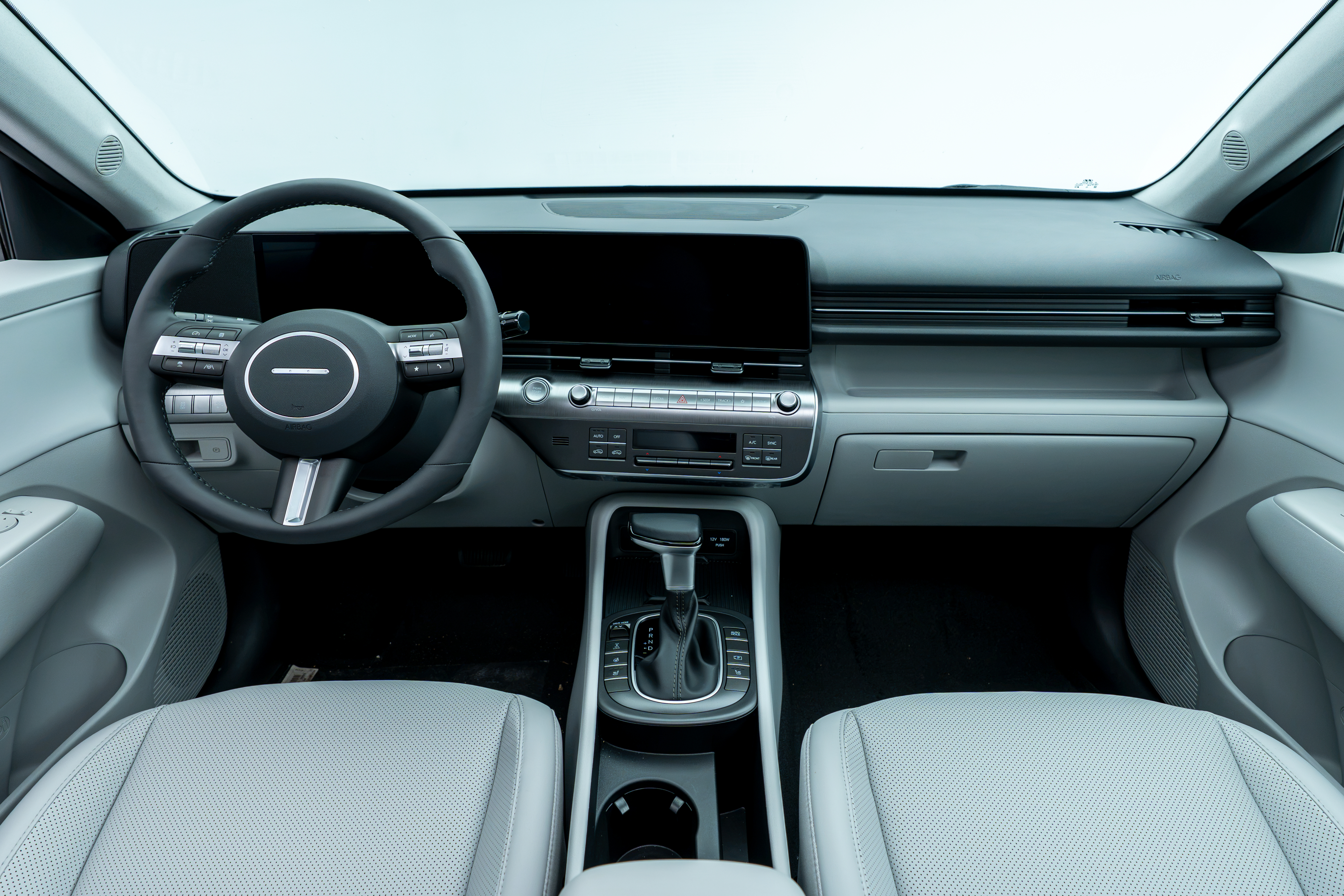 Interior view of a 2026 Hyundai Kona featuring the steering wheel, digital display, dashboard, centre console, and light-coloured front seats.
