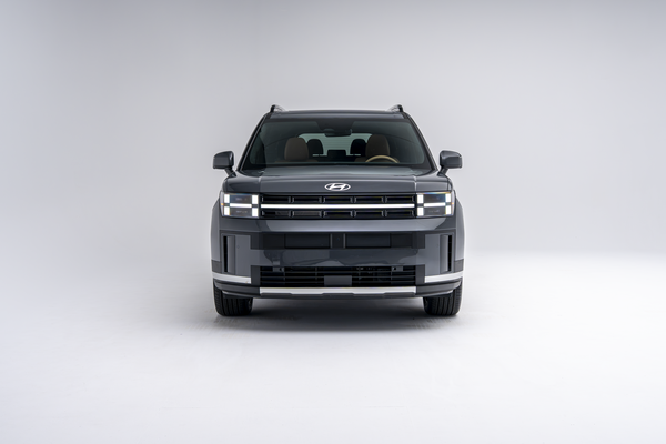 Front view of a grey 2026 Hyundai Santa Fe Hybrid SUV with LED headlights illuminated on a white studio background.