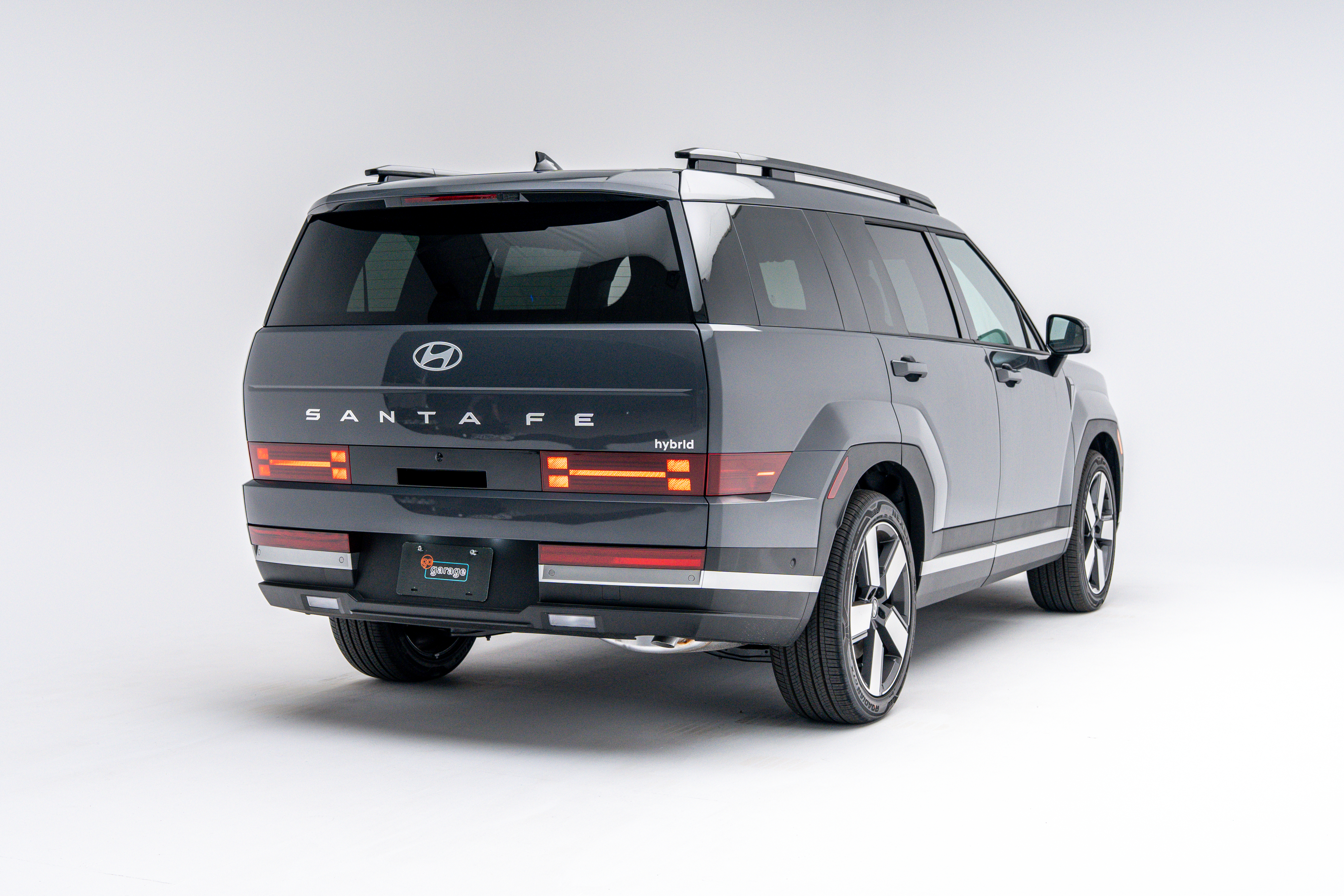 Rear three-quarter view of a grey 2026 Hyundai Santa Fe Hybrid SUV with LED taillights illuminated on a white studio background.