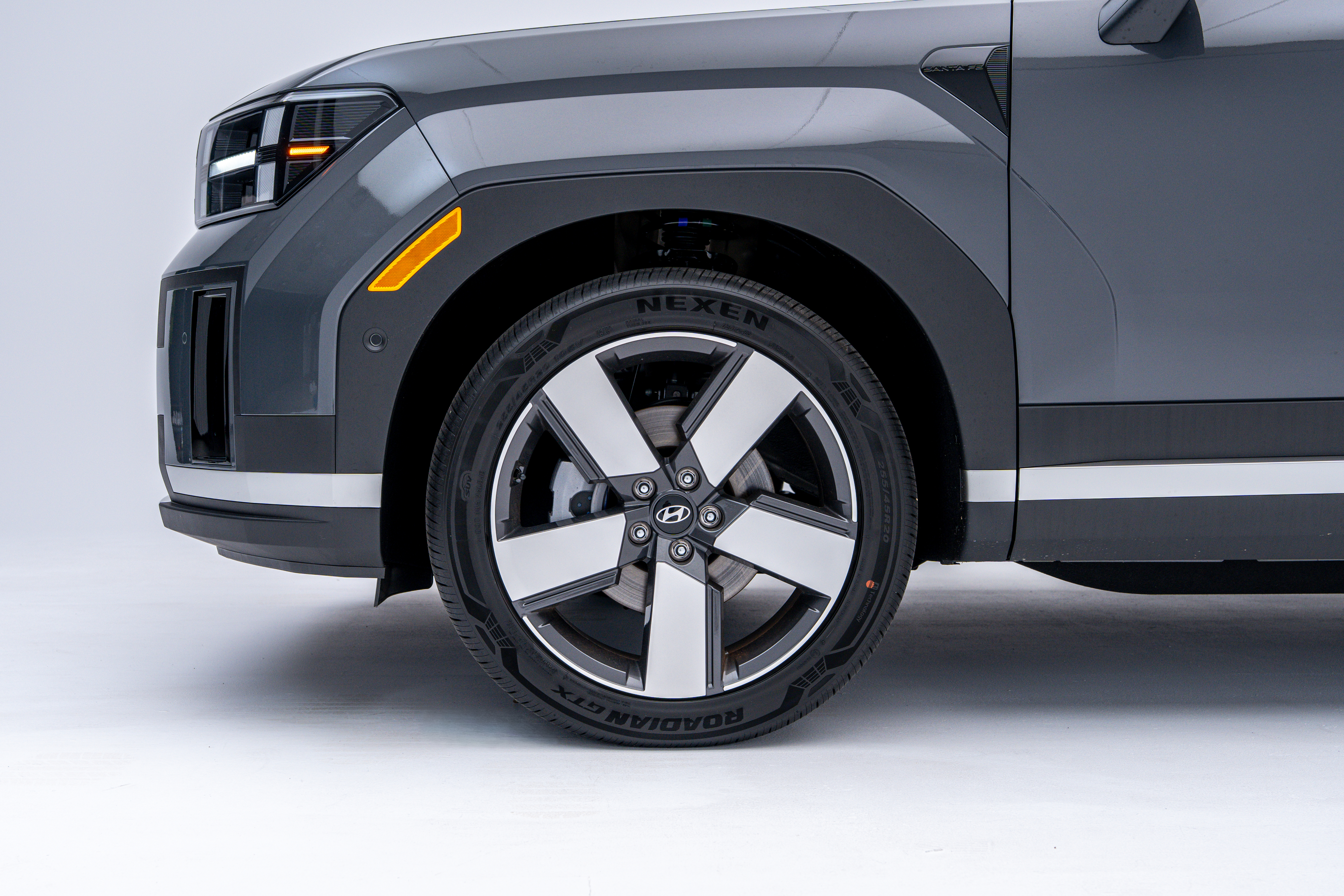 Close-up side view of the front wheel and fender of a grey 2026 Hyundai Santa Fe Hybrid, featuring a two-tone alloy wheel.