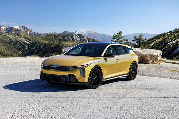 Yellow Kia K4 parked on gravel overlook with mountain range in background