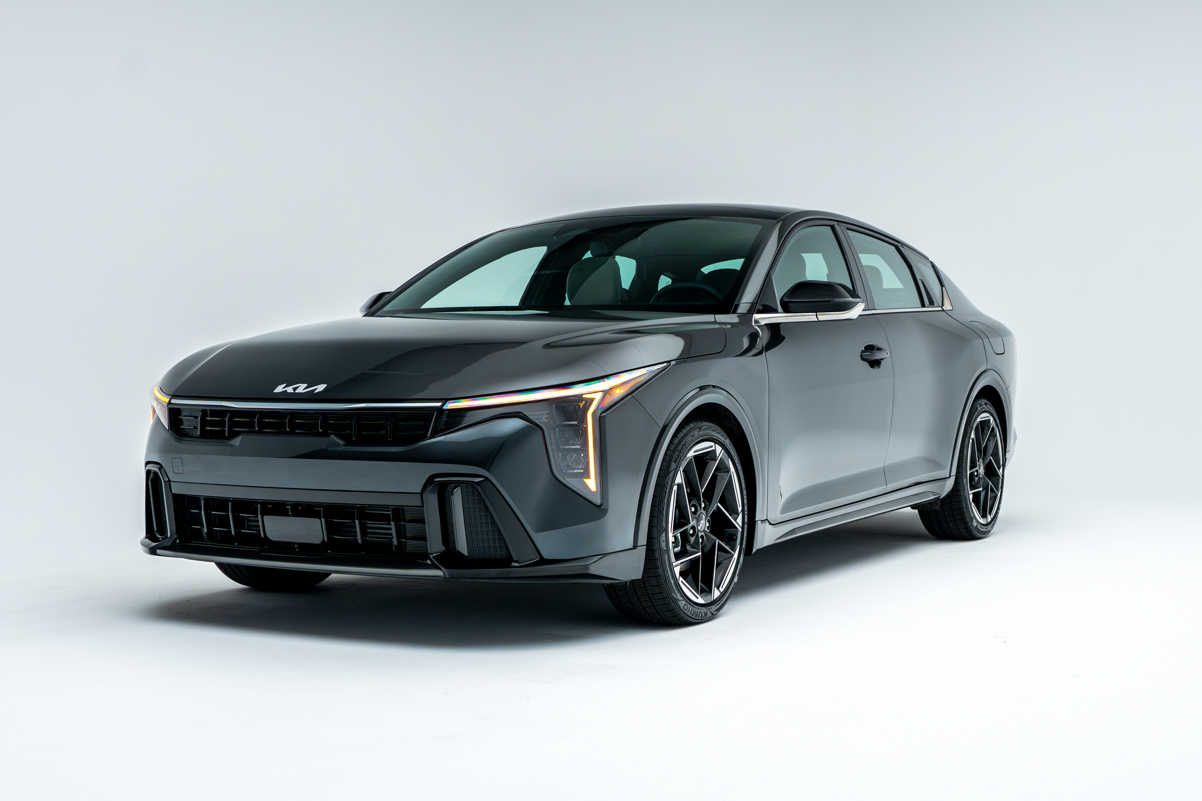 Front three-quarter view of a grey 2026 Kia K4 showing LED headlights, grille, alloy wheels and sedan profile.