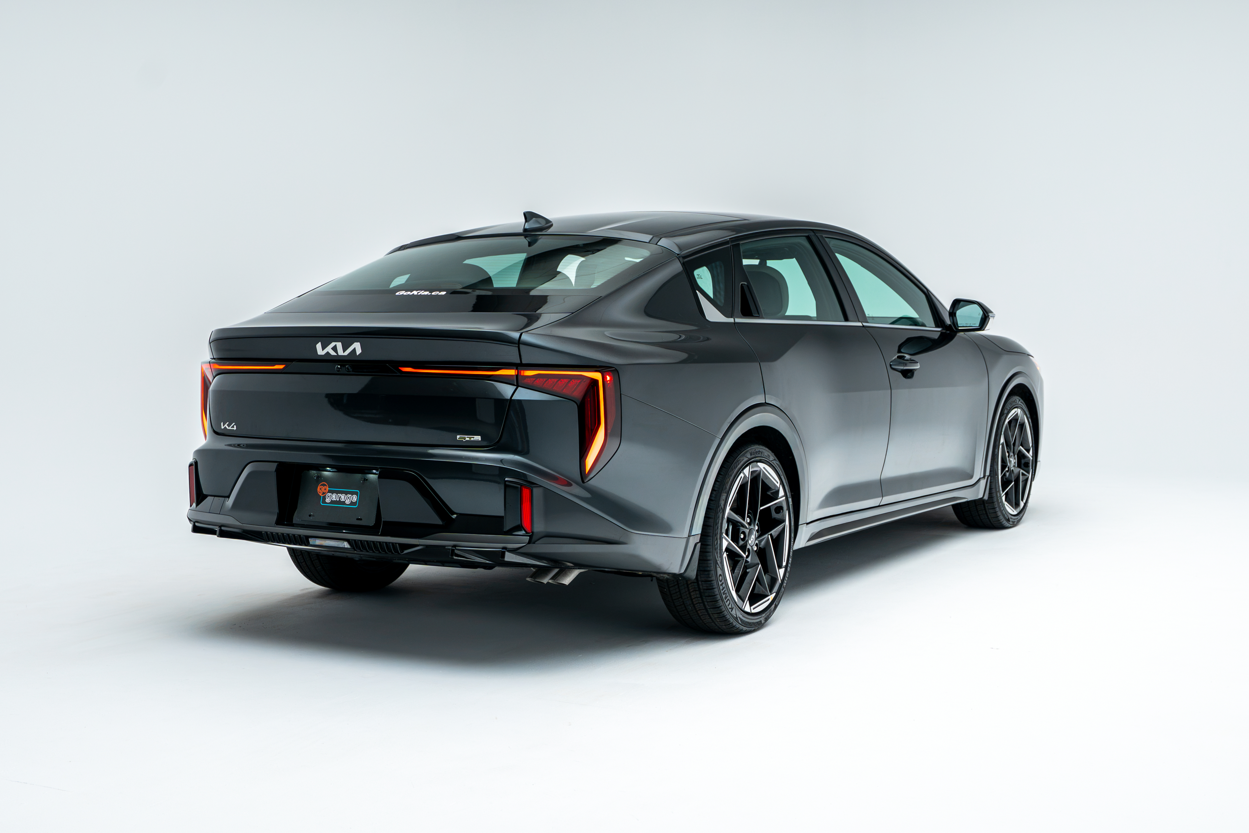 Rear three-quarter view of a grey 2026 Kia K4 showing LED taillights, alloy wheels and sedan profile.