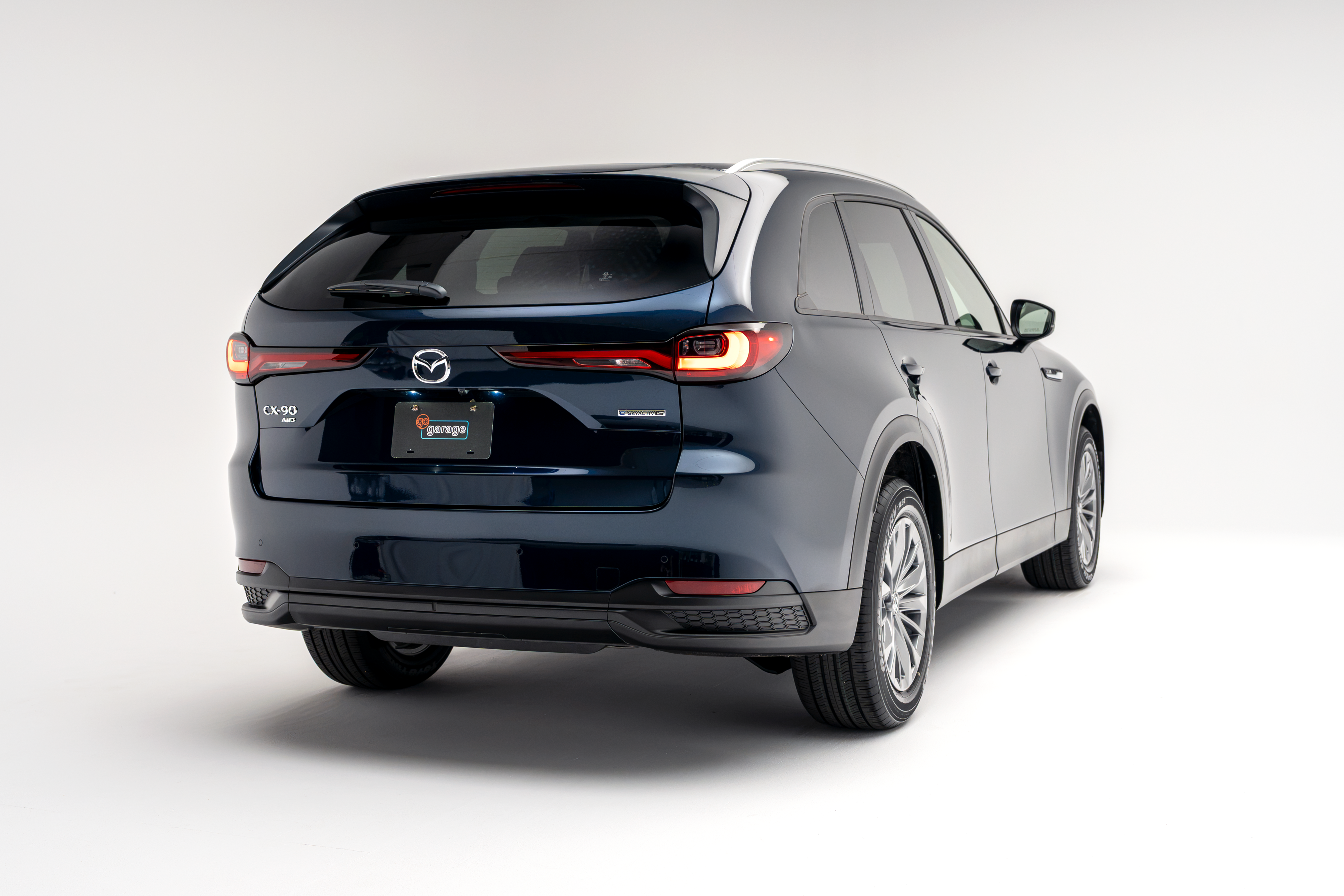Rear three-quarter view of a blue 2026 Mazda CX-90 showing LED taillights, alloy wheels and SUV profile.