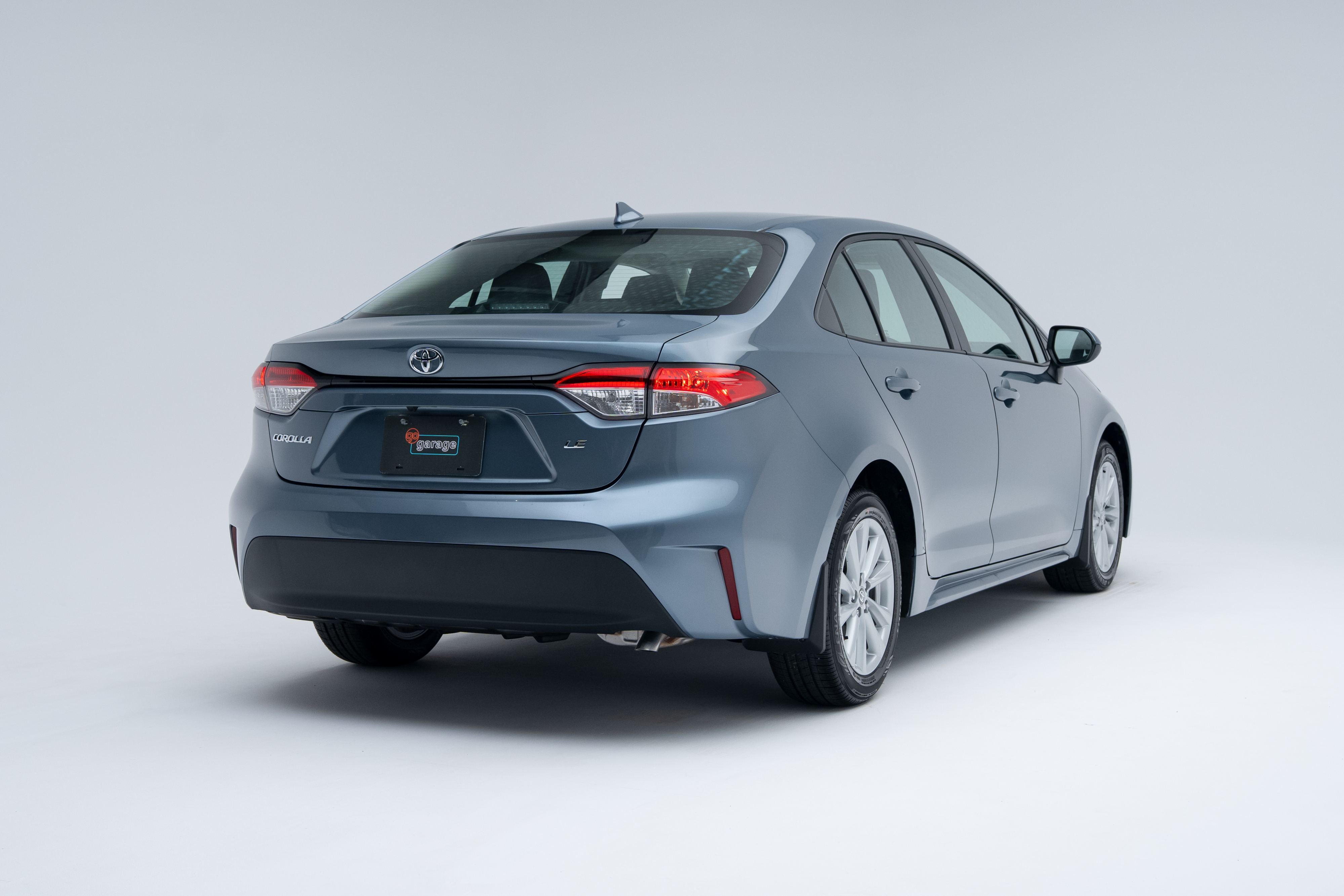 Rear three-quarter view of a light blue 2026 Toyota Corolla sedan on a white studio background.