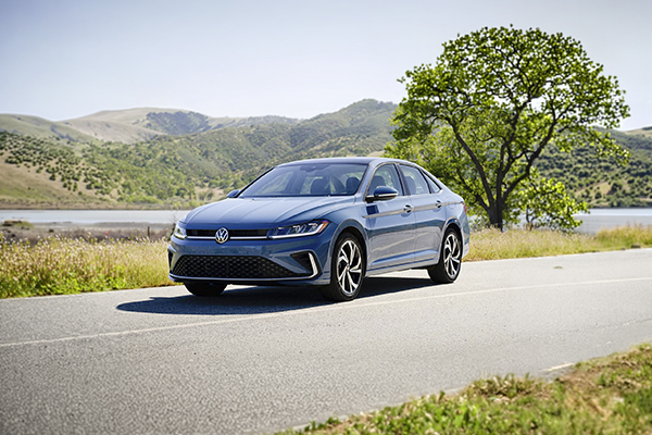 Volkswagen Jetta sedan parked on a road with scenic lake and mountain landscape in background