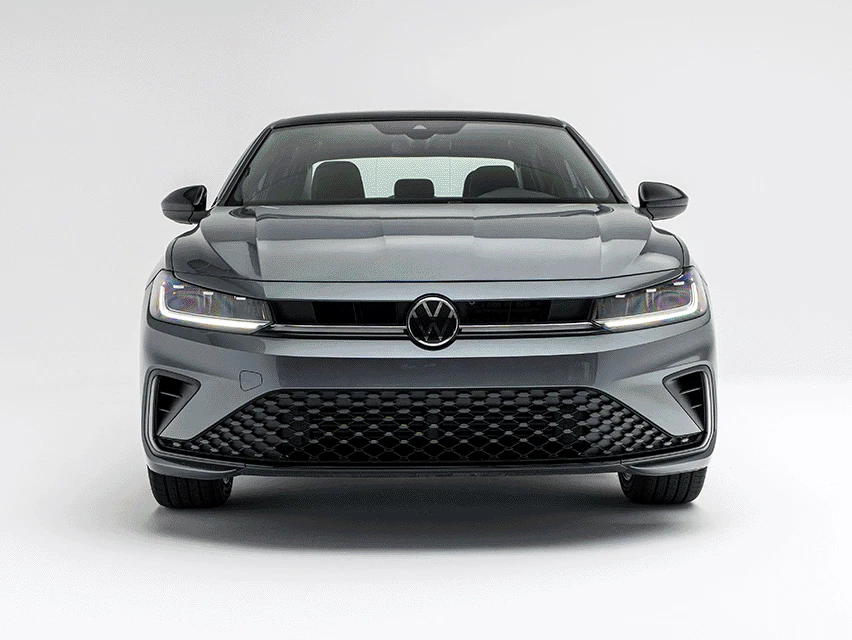 Front view of a grey Volkswagen Jetta with LED headlights illuminated against a white background.