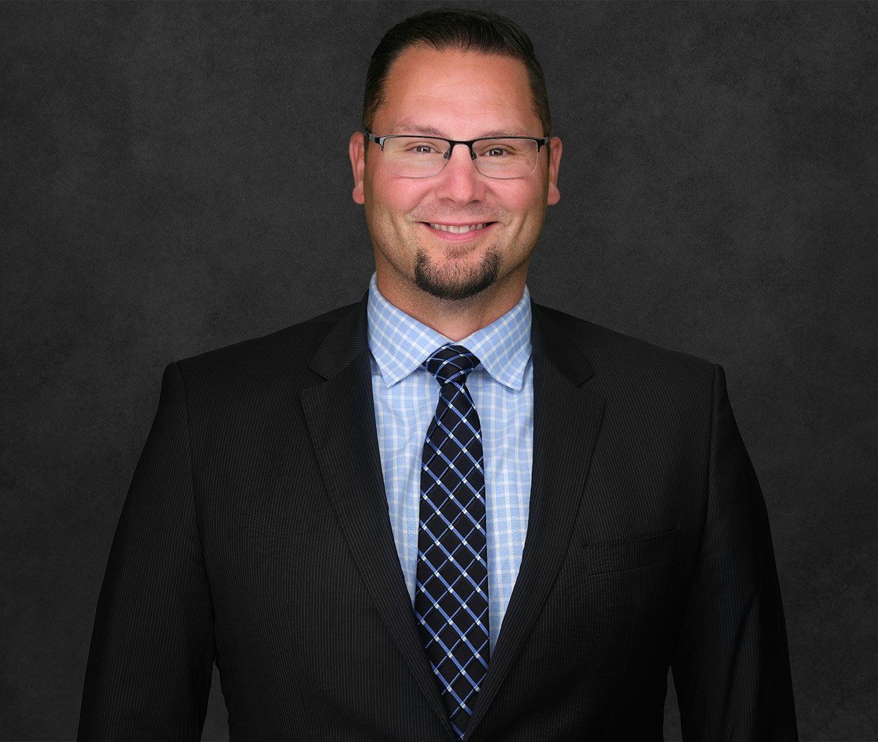 Mark Szott wearing glasses, a suit and tie, and smiling