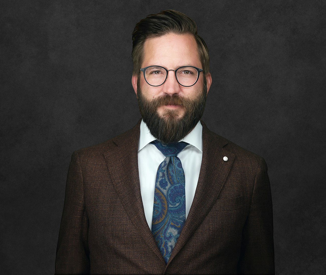 Phil Abram smiling, wearing glasses, a beard, a suit, white shirt and blue and green patterned tie