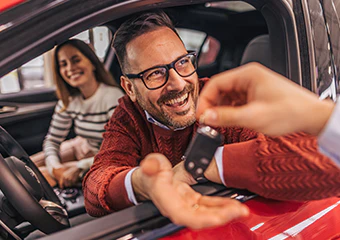 A man and woman in a car smiling getting the keys to their new car