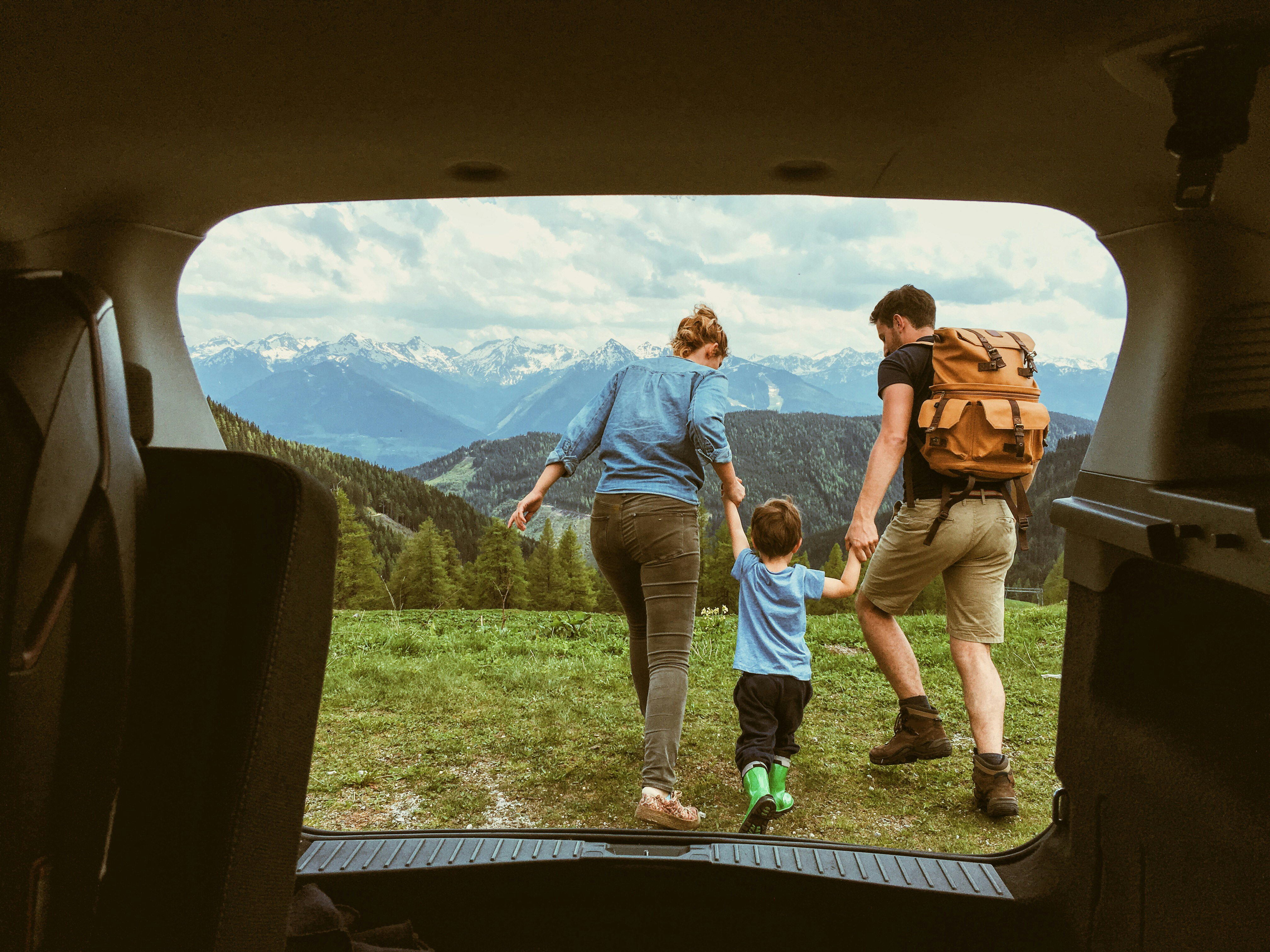 A view from inside a vehicle of a boy standing between a woman and man, holding hands and looking at the mountains