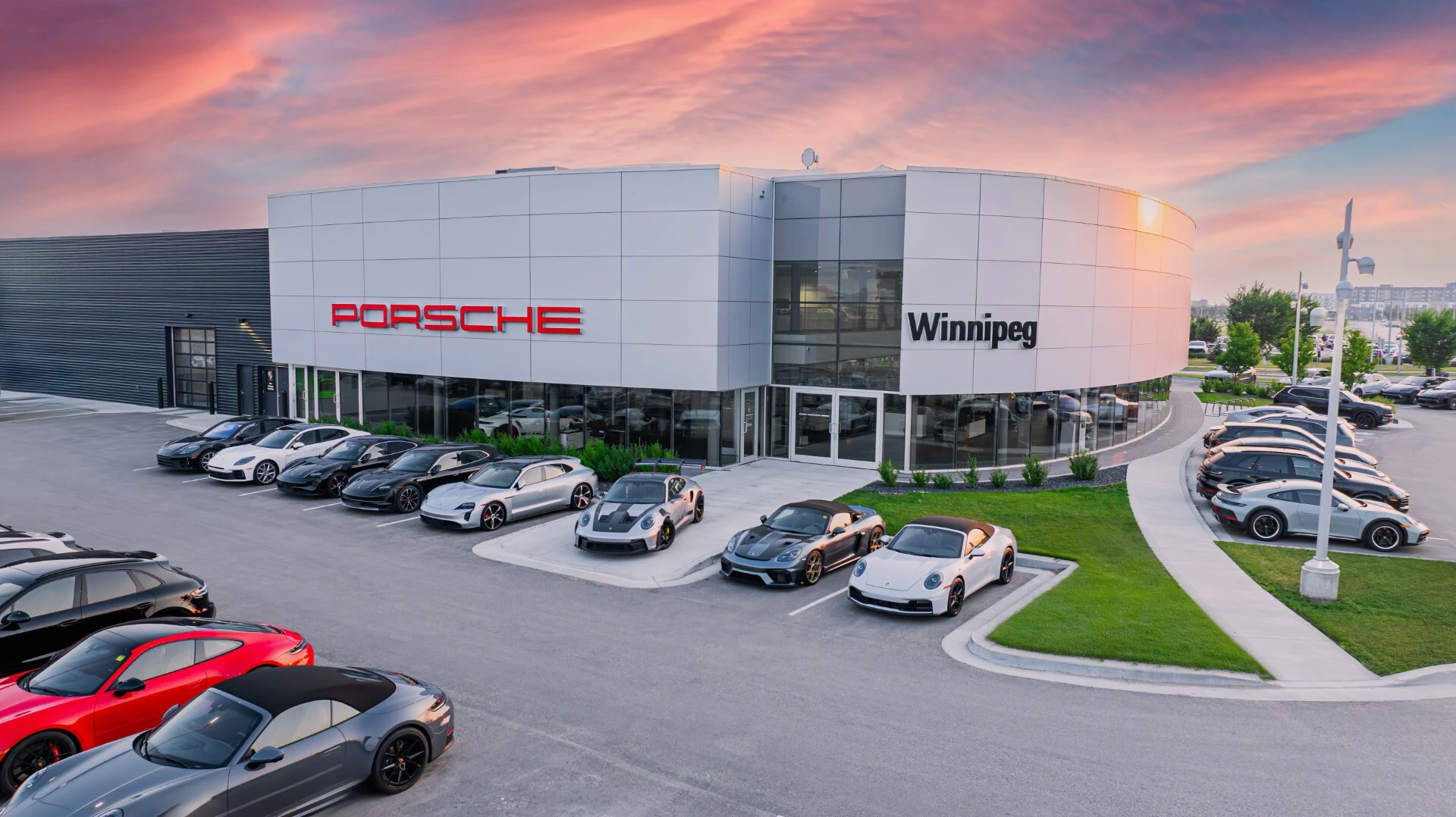 Porsche dealership exterior in Winnipeg with luxury sports cars displayed in front at sunset