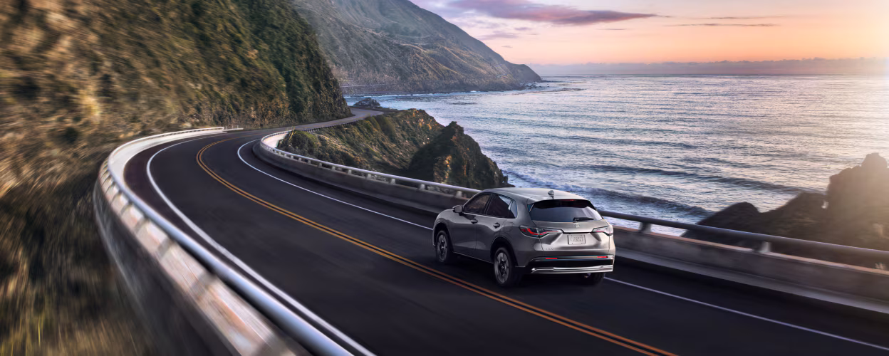 2026 Honda HR-V driving down a windy road by water.