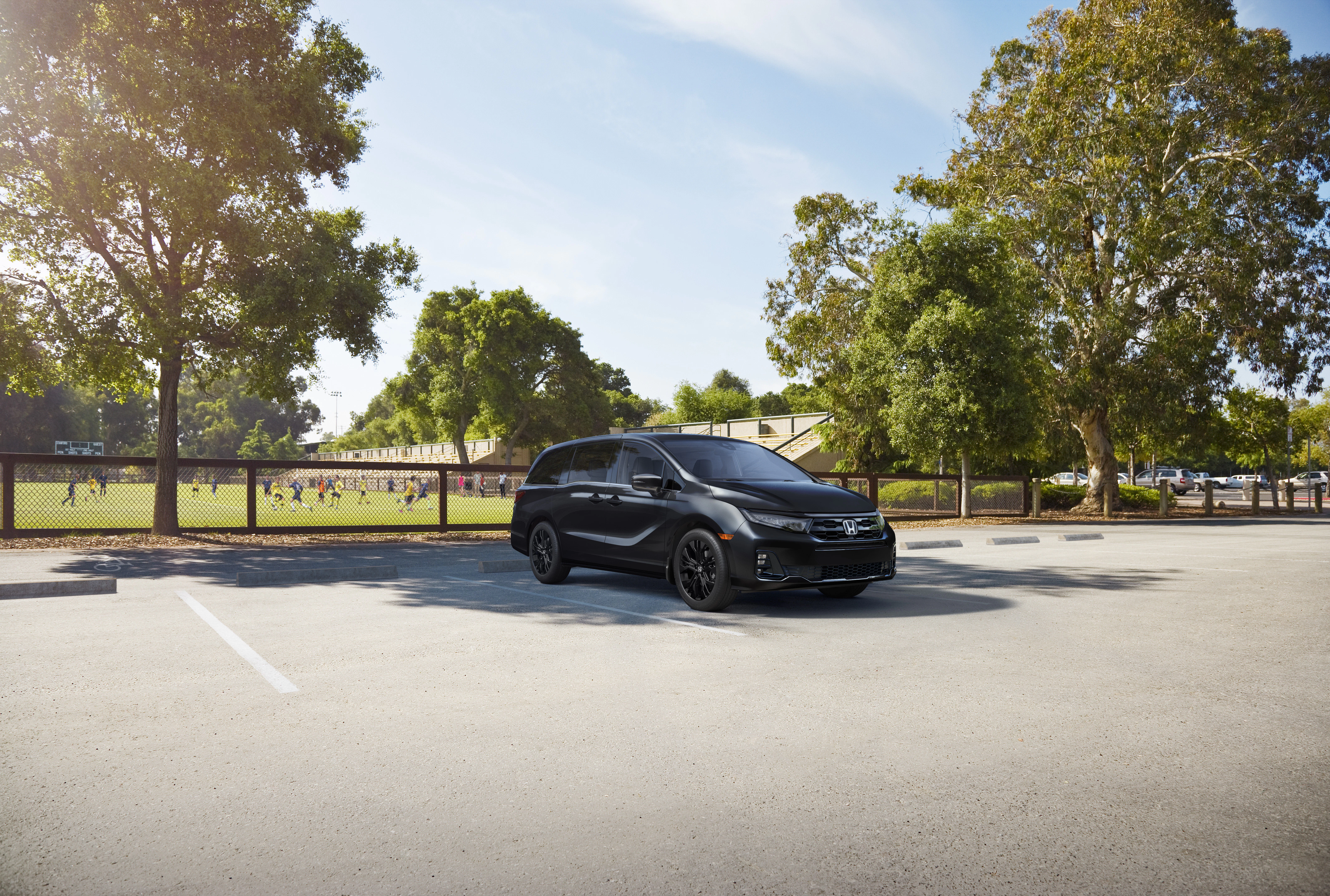 Honda Odyssey Black Edition parked beside a community sports field, highlighting everyday family practicality and a sleek, modern design.