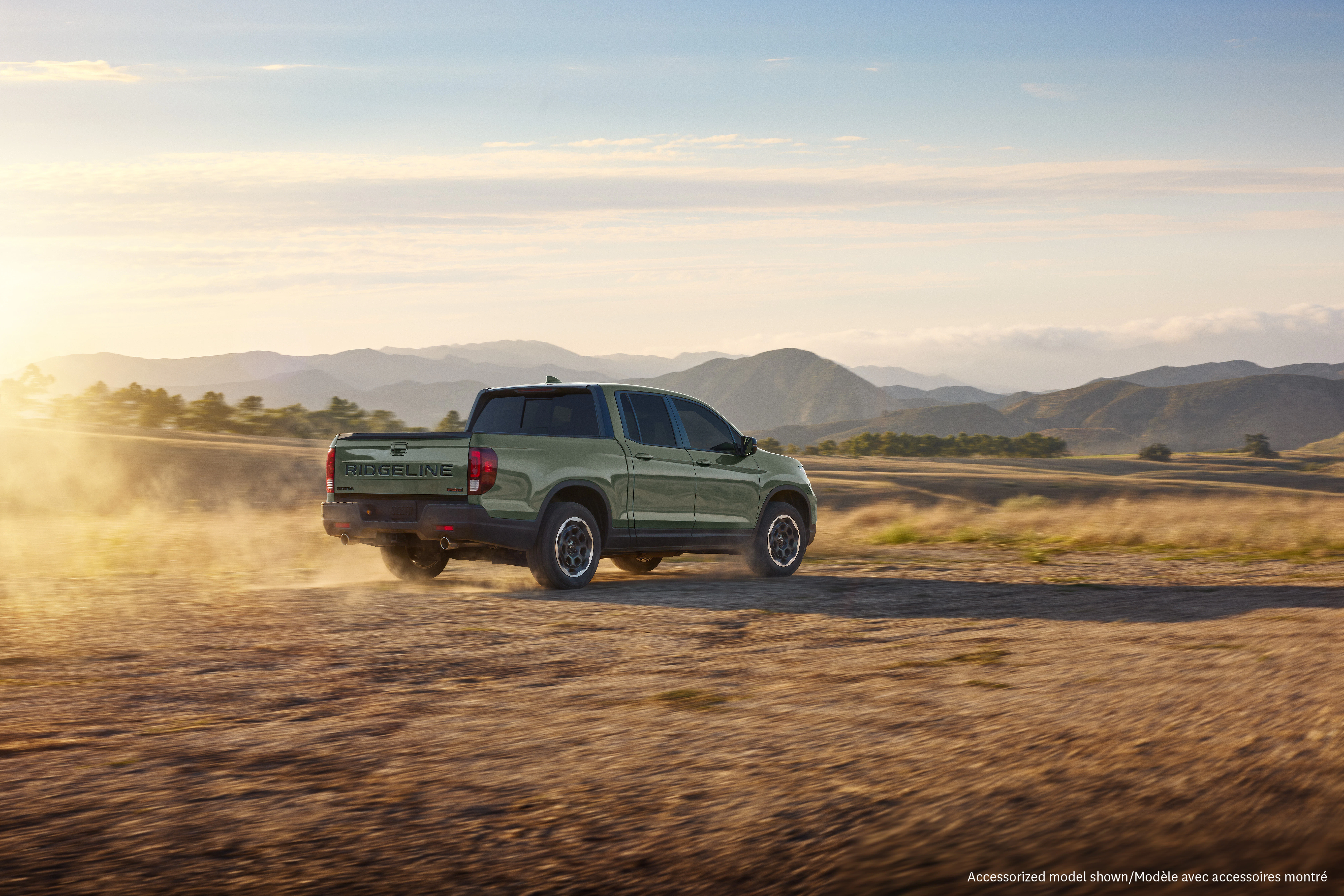 Honda Ridgeline TrailSport powers across a rugged dirt trail at sunset, showcasing off-road capability against a scenic mountain backdrop.