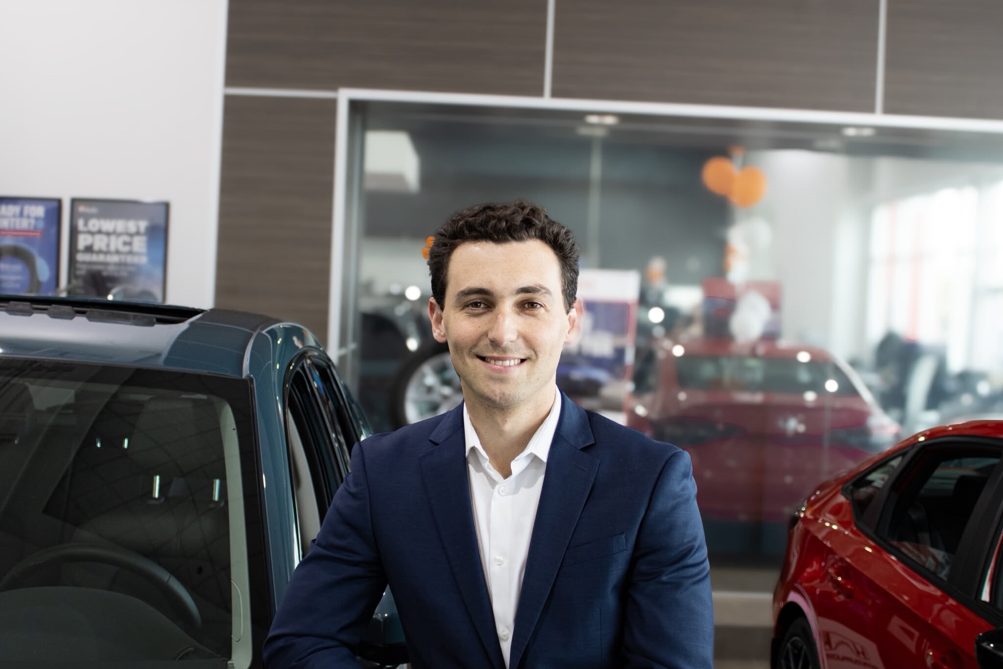 Go Auto sales representative smiling in dealership showroom with vehicles displayed behind him