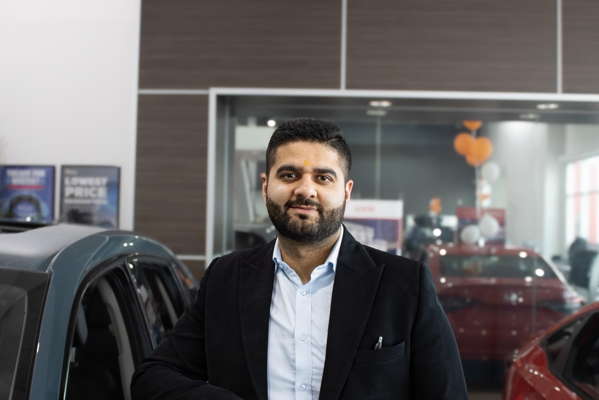 Car salesman standing in dealership showroom next to vehicle