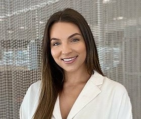 Nicole Lindsay is wearing a white shirt and smiling at the camera, with an office in the background.