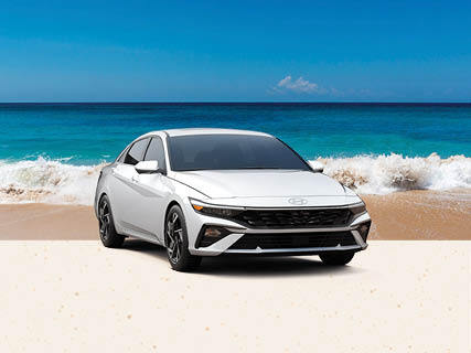 White Hyundai Elantra parked on a sandy beach beside turquoise water