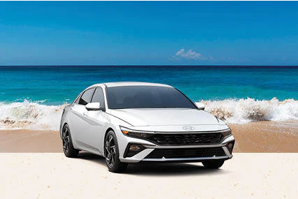 White Hyundai Elantra parked on a sandy beach beside turquoise water