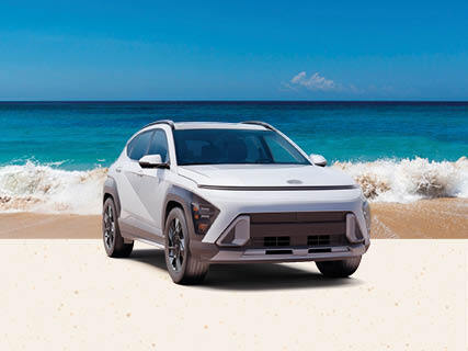 White Hyundai Kona parked on beach with ocean waves in background