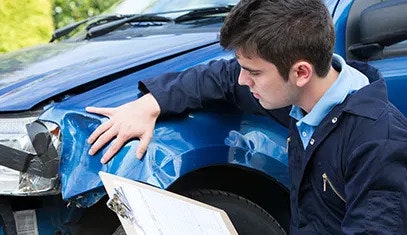 A man holding a clipboard and inspecting damage to the front of a vehicle