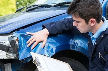 A man holding a clipboard and inspecting damage to the front of a vehicle