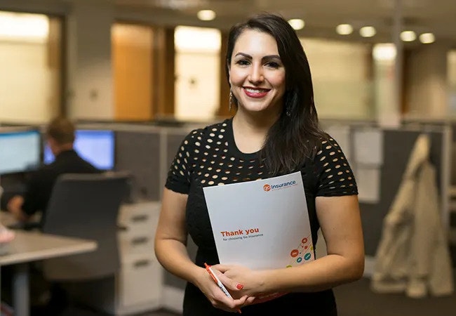 A woman in an office, smiling at the camera and holding a Go Insurance-branded document
