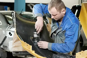 A man in protective clothing, holding a screwdriver and working on a headlight