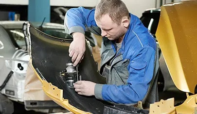 A man in protective clothing, holding a screwdriver and working on a headlight