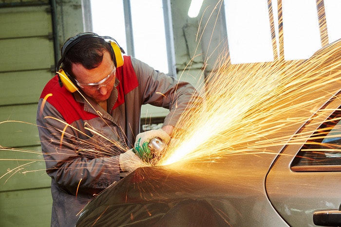 A man wearing protective clothing and ear muffs, grinding a vehicle