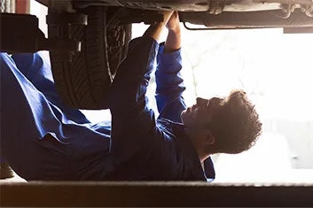 A man in blue overalls is lying underneath a raised-up vehicle, servicing it