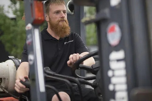 A man with a beard is driving a forklift truck