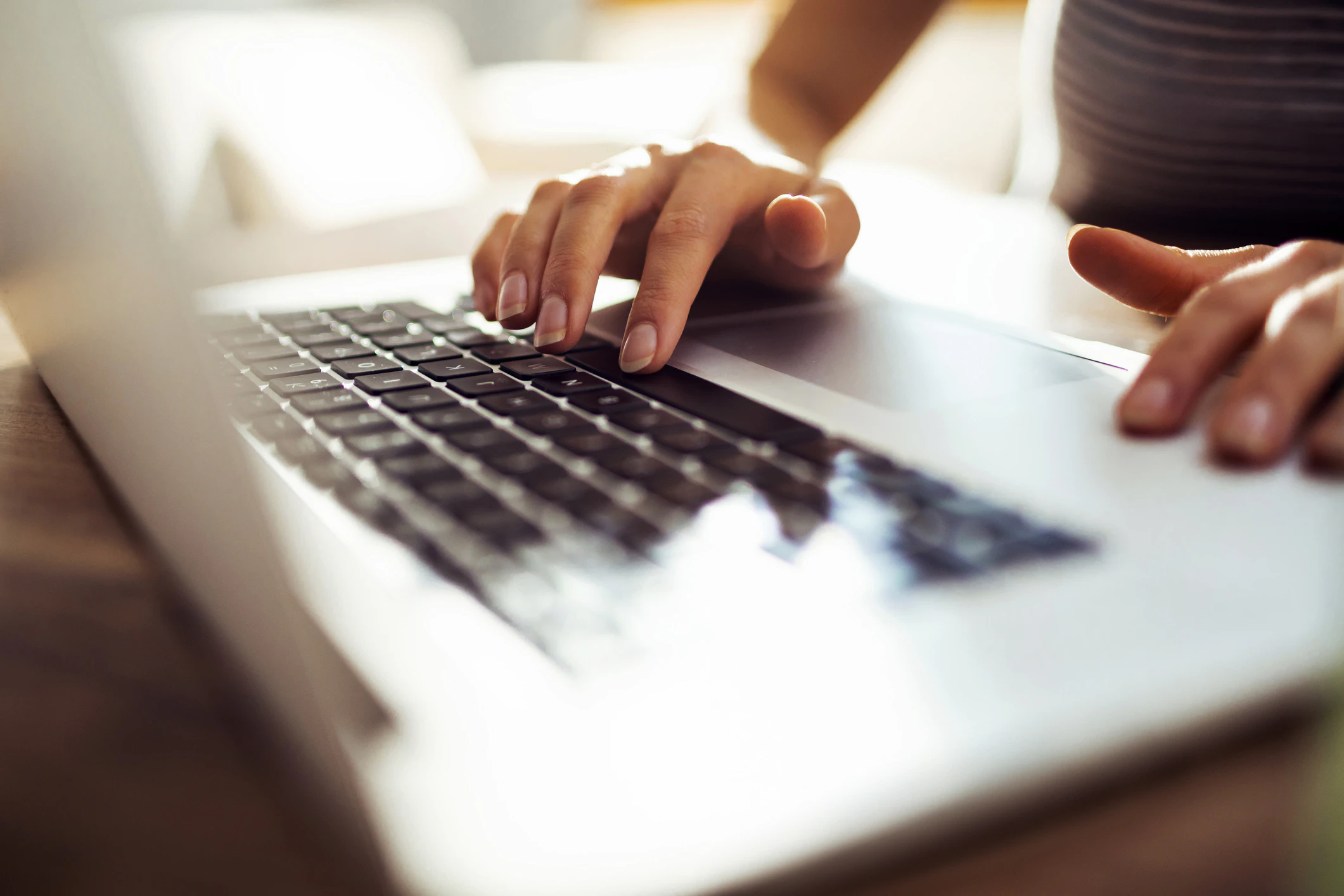 Two hands are on an open laptop. One hand is resting the index finger on the other hand is pressing the space bar