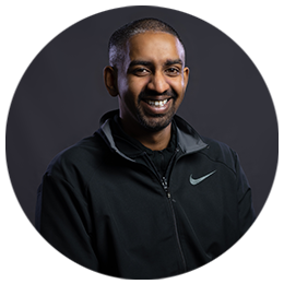 Thejus Swamy standing side-on, wearing a black zip-up hooded fleece and smiling