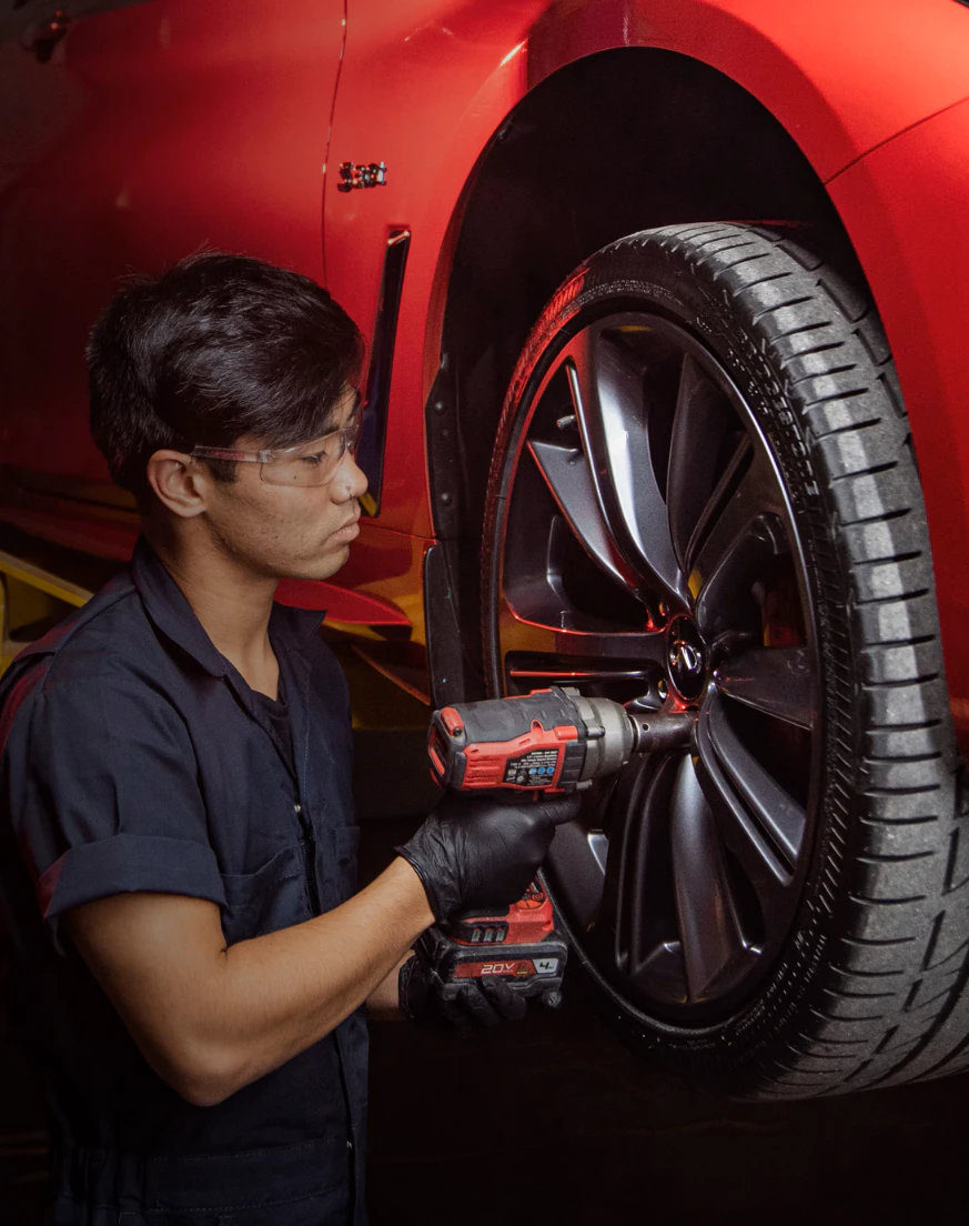Service technician removing lug nuts from red vehicle wheel with impact driver