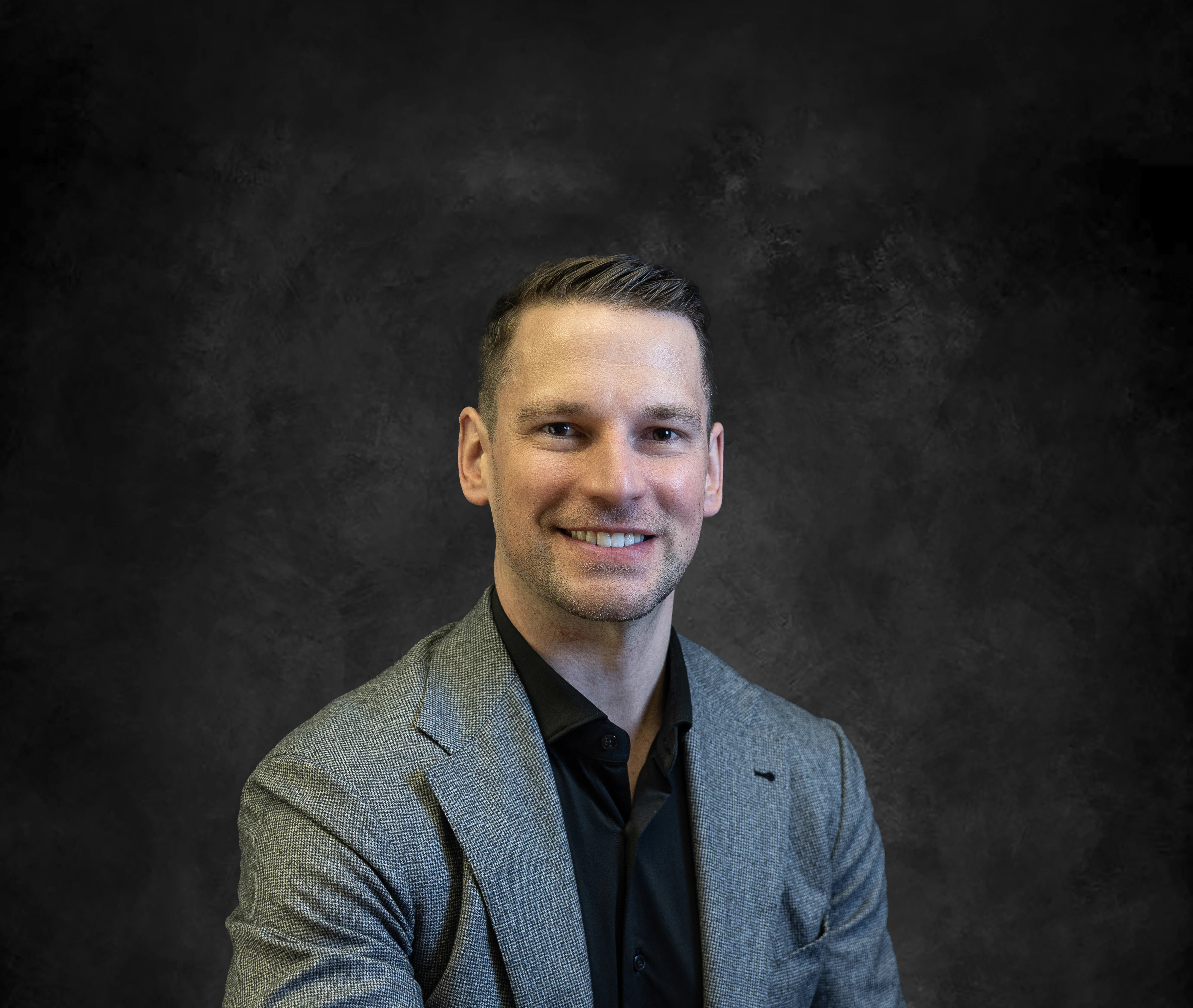Professional headshot of man in gray blazer at desk