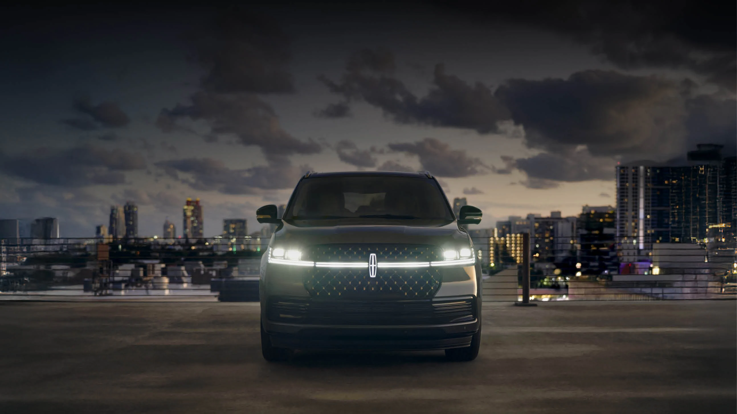 Lincoln SUV with illuminated grille parked on rooftop overlooking city skyline at dusk